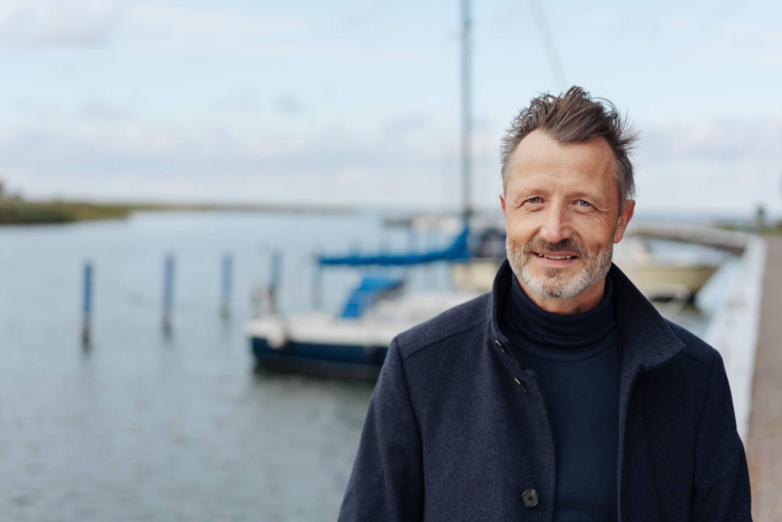 Man taking a stroll on a waterfront promenade in a warm overcoat on a cold autumn day in a close up portrait